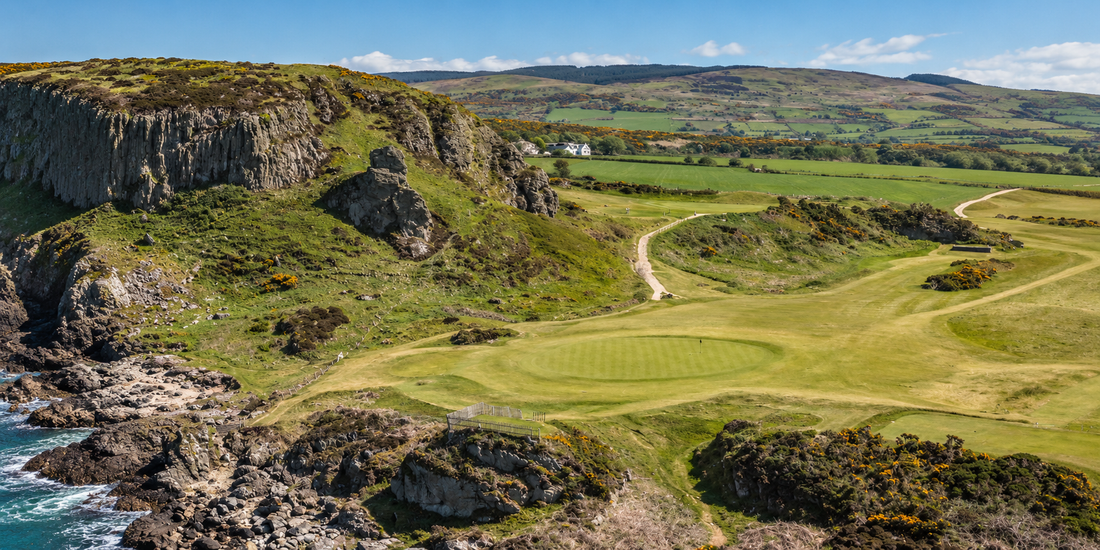 Shiskine Golf Club on the Isle of Arran, with a coastal green beneath rocky cliffs and rolling hills beyond
