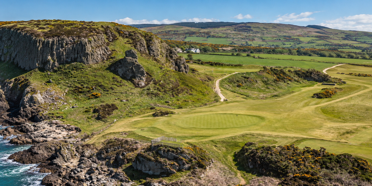 Shiskine Golf Club on the Isle of Arran, with a coastal green beneath rocky cliffs and rolling hills beyond